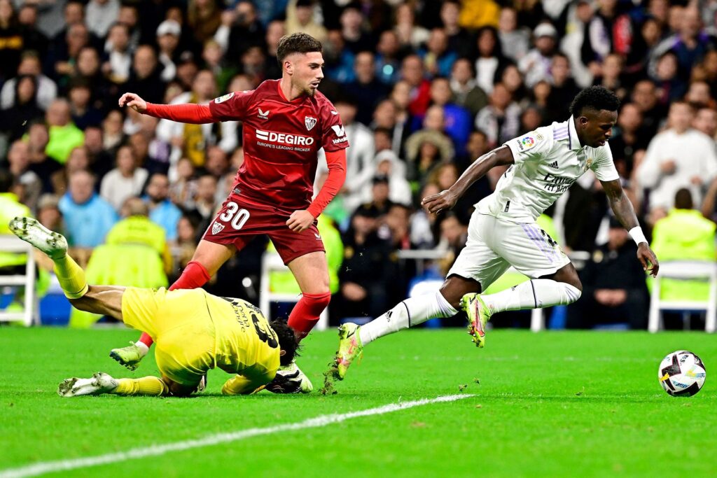 Real Madrid's Brazilian forward Vinicius Junior (R) fights for the ball with Sevilla's Spanish defender Jose Angel Carmona (L) and Sevilla's Moroccan goalkeeper Yassine Bounou "Bono" (Down) during the Spanish league football match between Real Madrid CF and Sevilla FC at the Santiago Bernabeu stadium in Madrid