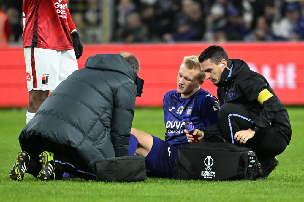 Kasper Dolberg sidder i græsset i den lilla trøje og ømmer sig efter en skade for Anderlecht