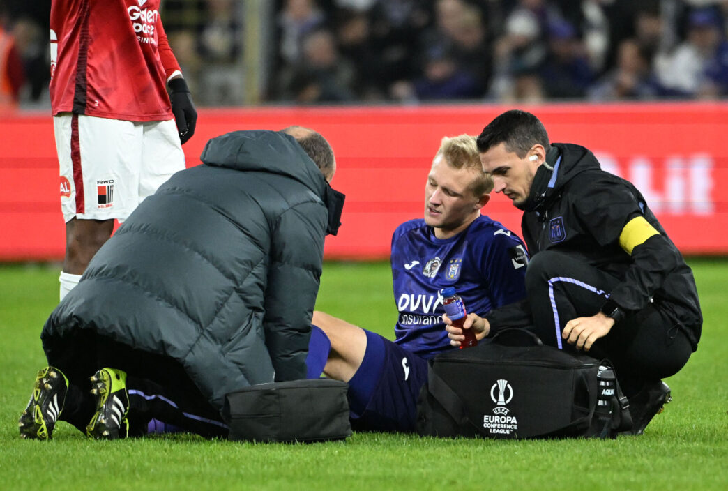 Kasper Dolberg sidder i græsset i den lilla trøje og ømmer sig efter en skade for Anderlecht