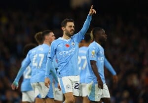 Bernado Silva med en løftet finger i Manchester Citys blå trøje.