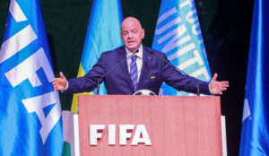 Infantino står med armene ude foran en desk