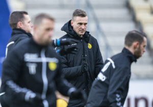 Mads Lyng står i ført en sort jakke og skuler gennem nogle spillere