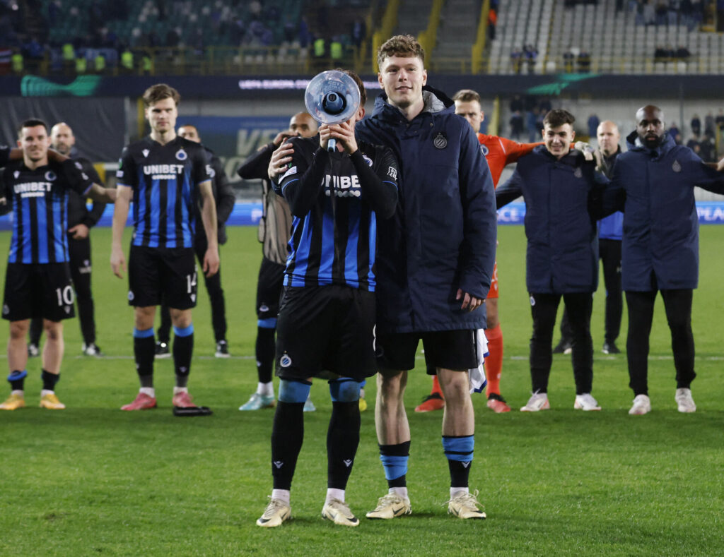 Andreas Skov Olsen står sammen med en holdkammerat fra Club Brugge, der står med en megafon.