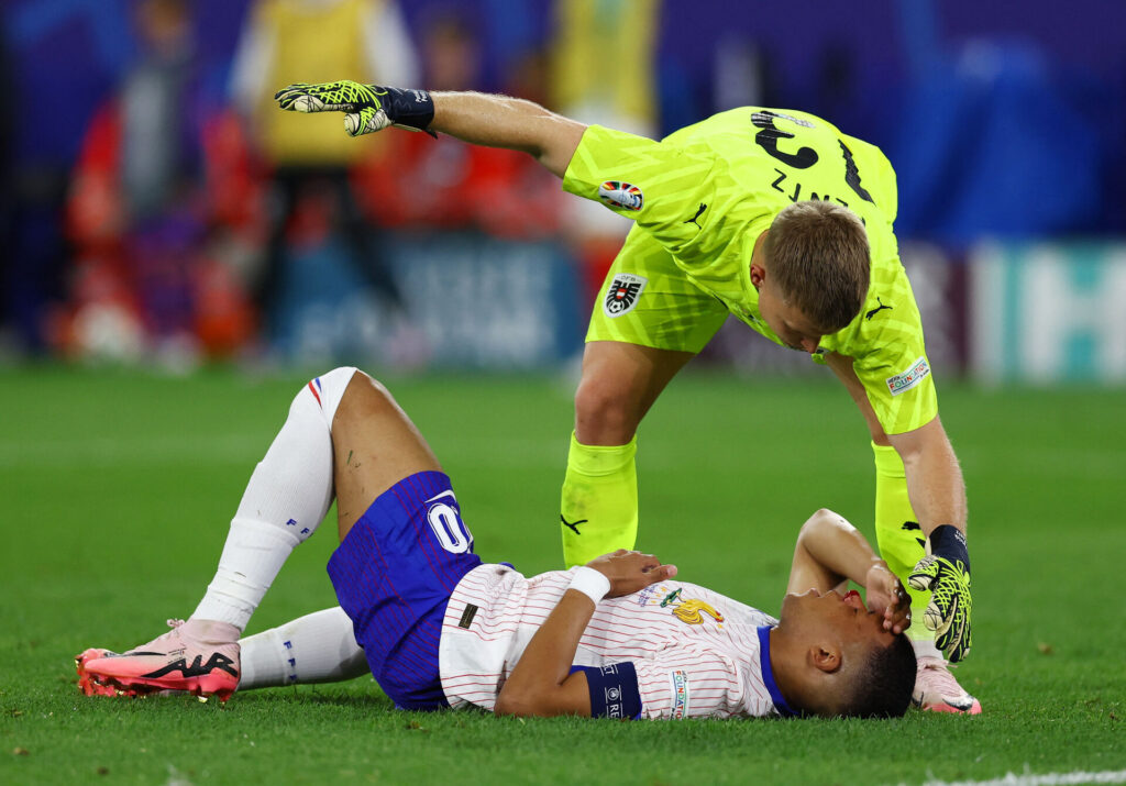 Kylian Mbappé ligger på græsset med en formodet brækket næse, imens Patrick Pentz kalder på hjælp.