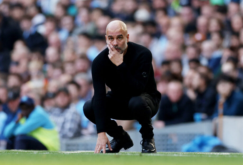 Pep Guardiola sidder på hug på sidelinkjen for Manchester City.