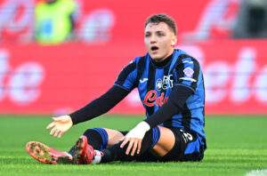 Mateo Retegui sidder på fodboldbanen og slår ud med armene.