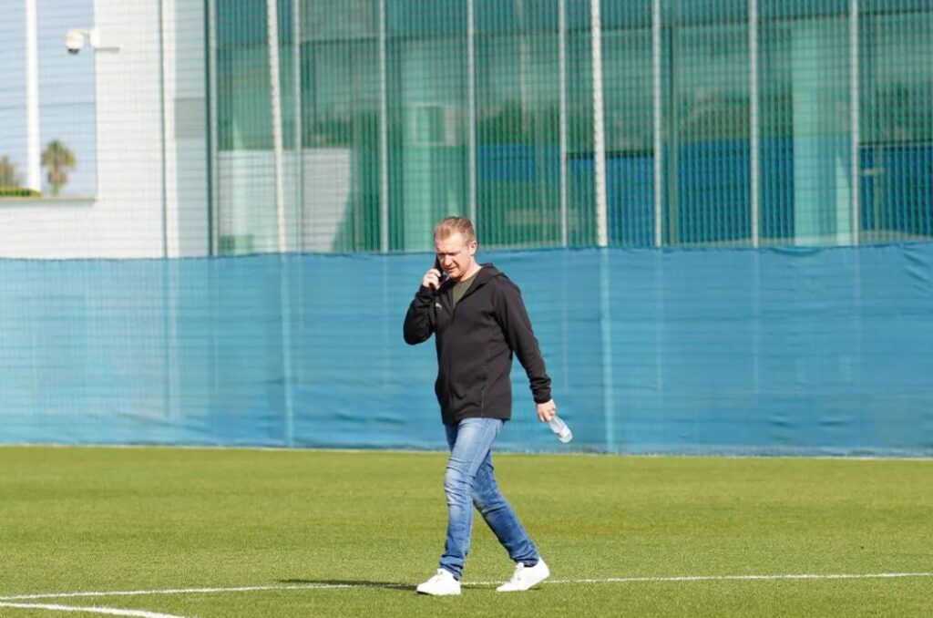 Randers FC-sportsdirektøren Sørensen Pedersen taler i telefon midt på træningsbanen.