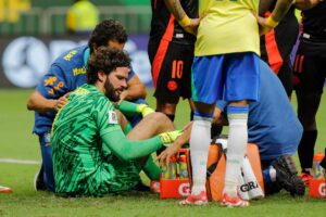 Alisson sidder i græsset og får behandling under en landskamp for Brasilien.