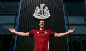 Dan Burn med udstrakte arme med Newcastle logo i baggrunden.