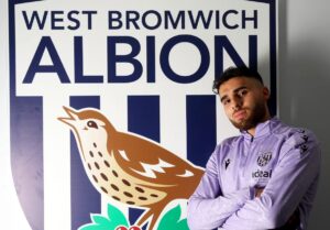 Tammer Bany med korslagte arme foran et WBA logo.