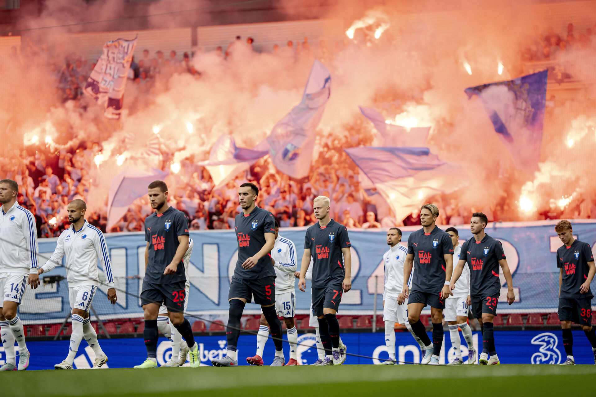 Malmos spillere løber på banen akkompagneret af romerlys fra fans.