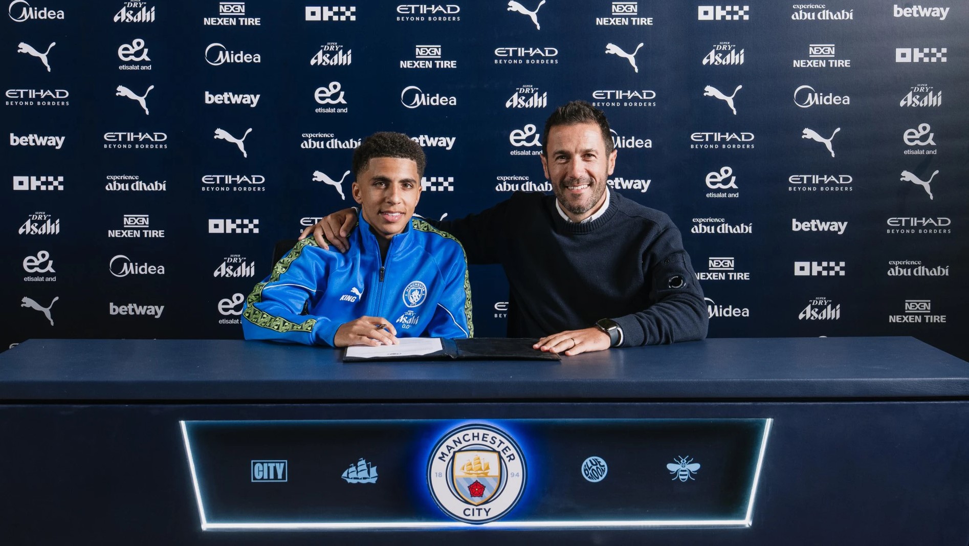 Rico Lewis skriver under på sin kontraktforlængelse på bordet foran sig.