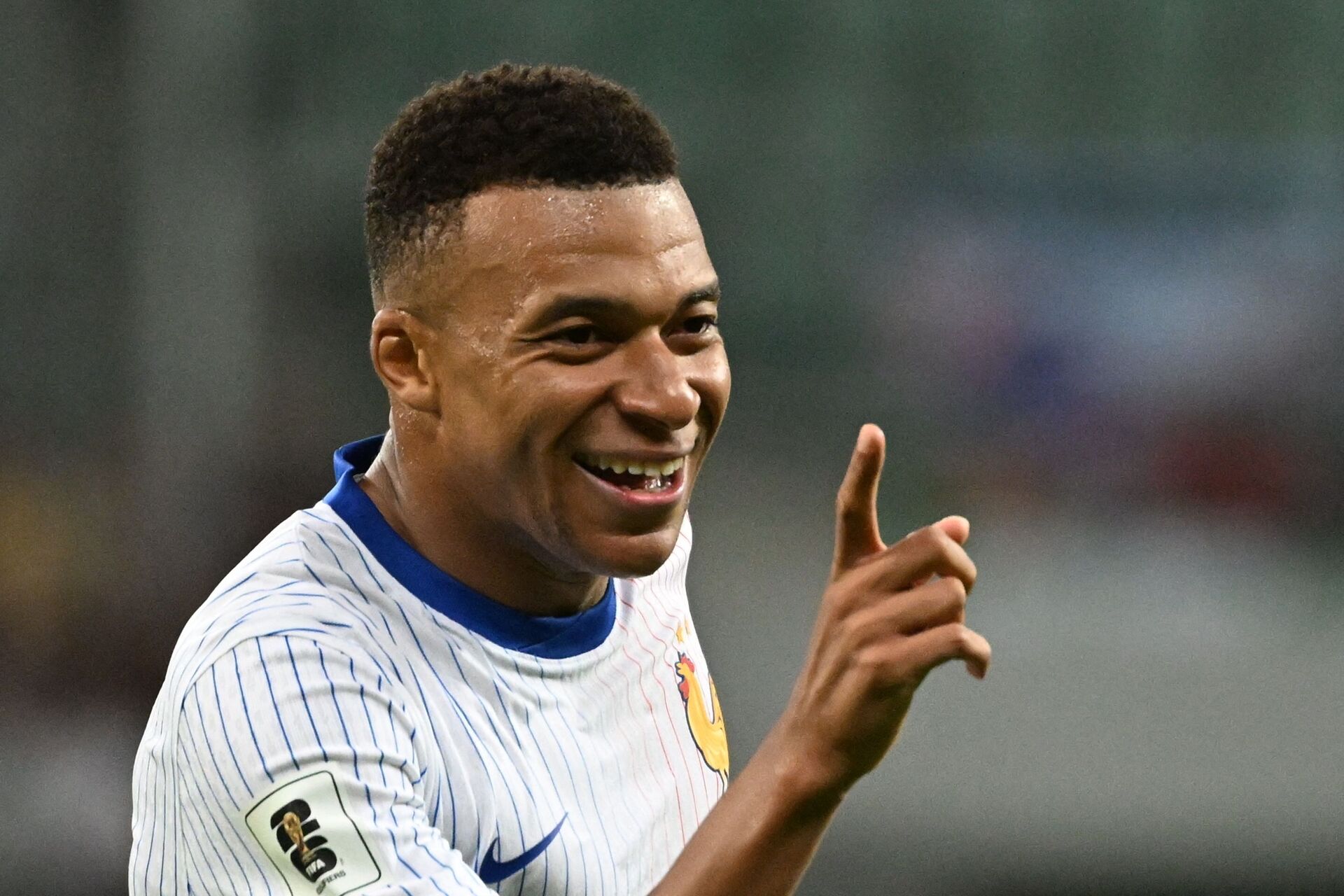 Kylian Mbappé med et stort smil og en løftet pegefinger.