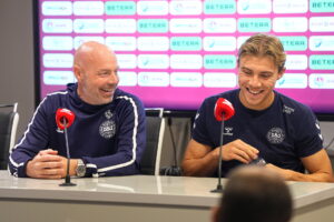 Brian Riemer sidder og smiler til Rasmus Højlund, der også smiler.