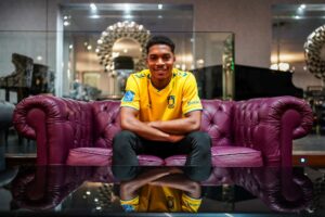 Justin Ché sidder i en bordeaux-farvet sofa iklædt en Brøndby-trøje.