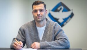 Tobias Thomsen skriver under på en kontrakt med et HB Køge logo i baggrunden.