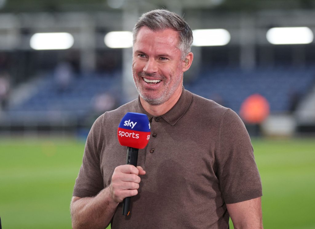Jamie Carragher står med en mikrofon og smiler.